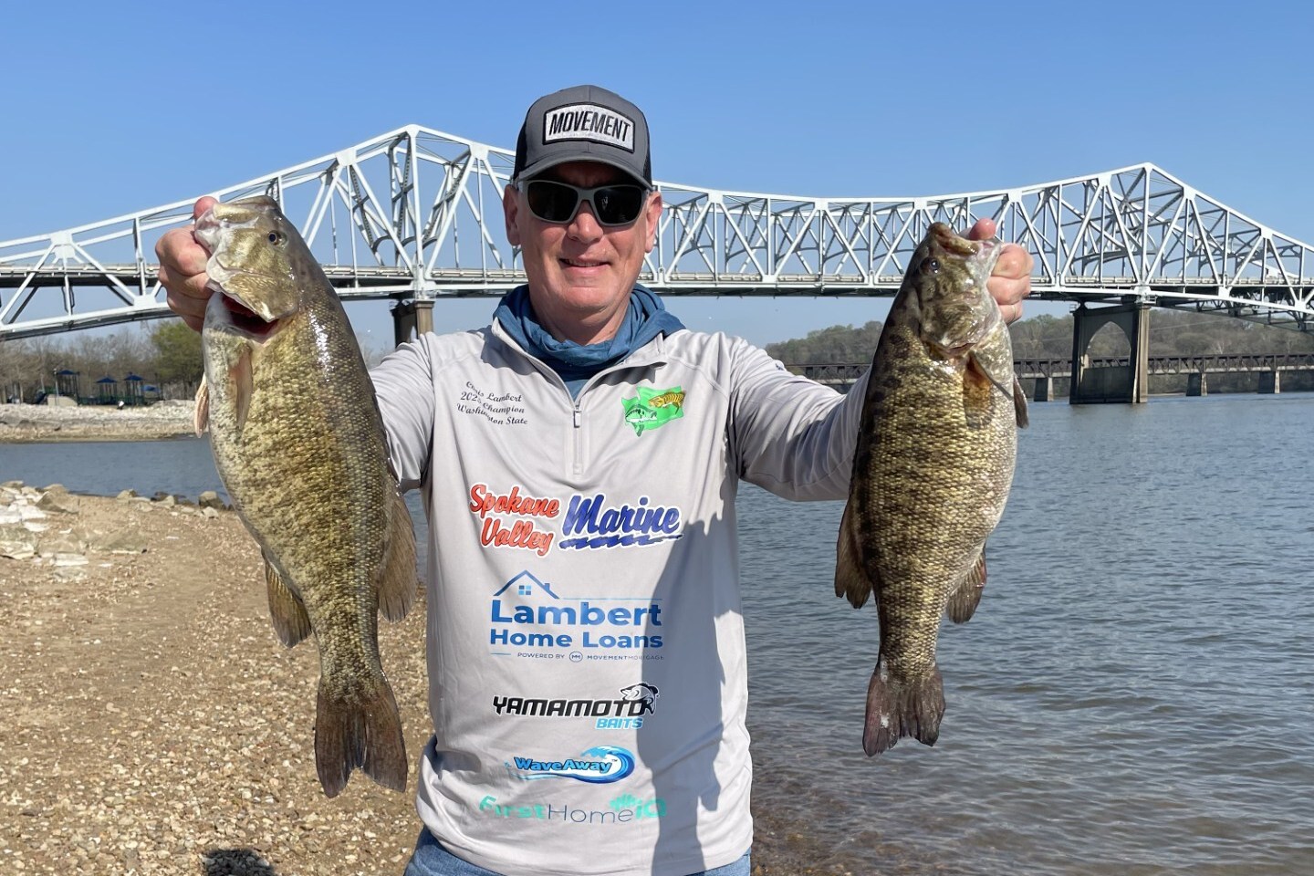 Chris Lambert holding two bass beside the water