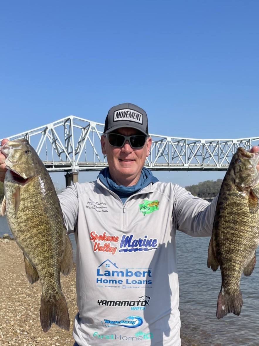 Chris Lambert holding two bass beside the water